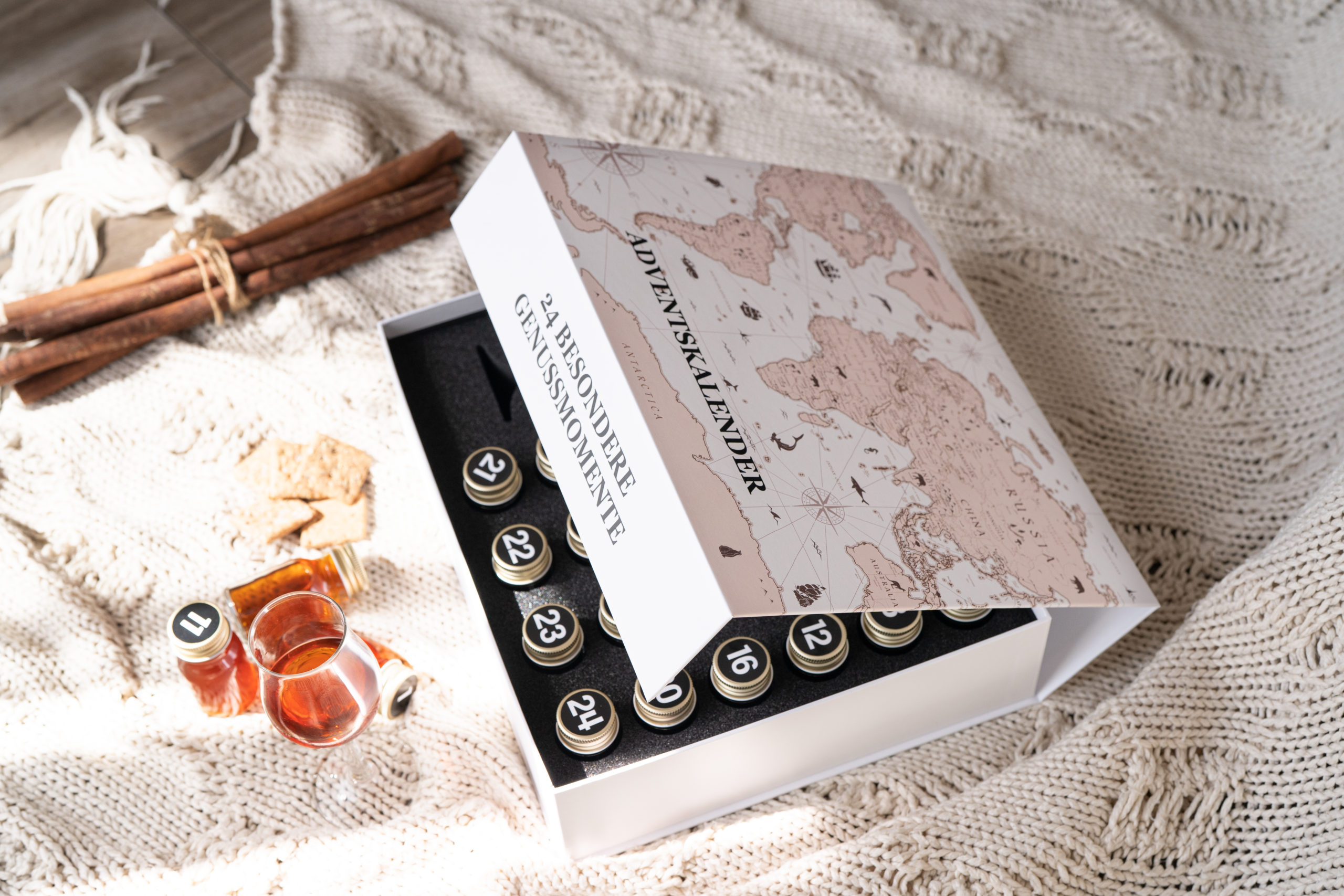 Halb geöffnete Tasting Box von Achilles mit Deko und Glas daneben und mit Druckveredelung einer Weltkarte Verpackung für Produktproben oder Adventskalender